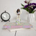 Decorative angel figurine with flowers on a book, with a clock and flowers in the background.