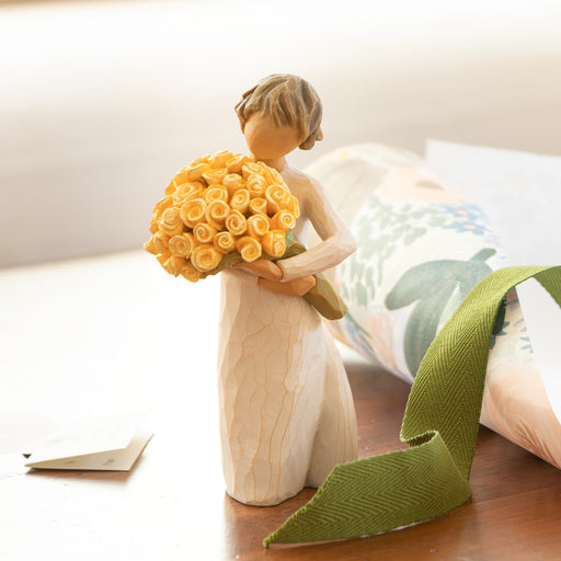 Standing figure in cream dress, holding large bouquet of yellow roses in her arms