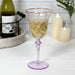 Decorative wine glass with floral pattern on a white surface with candles and a bottle in the background.