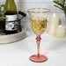 Pink wine glass with floral design filled with a clear liquid, bottle, and candles in the background.