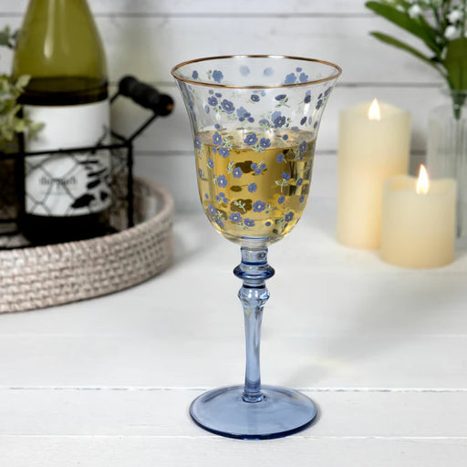 Decorative glass with floral pattern on a table with candles and bottles in the background