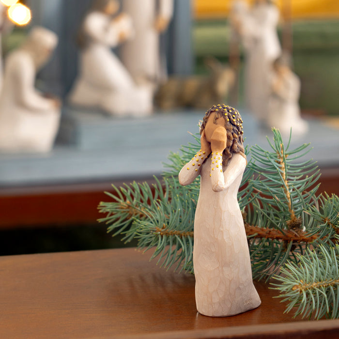 Decorative angel figurine with a child on a branch, surrounded by greenery on a wooden surface.