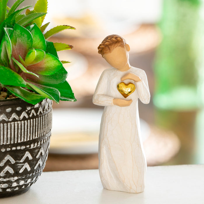 Decorative figurine of a woman holding a gold heart next to a potted plant.