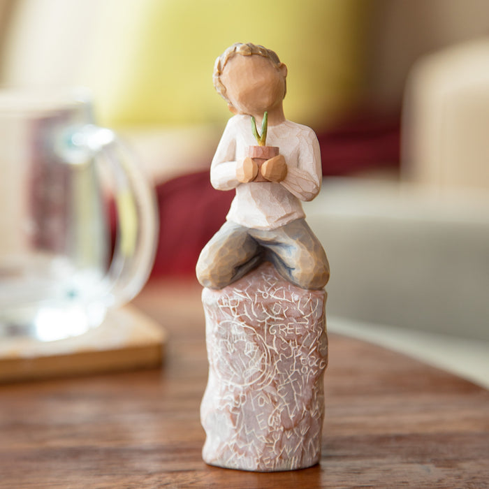 Ceramic figurine of a child holding a plant on a wooden surface