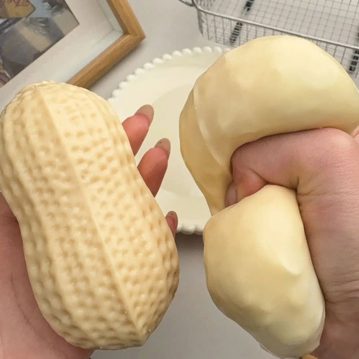 Two hands holding a novelty squishy toy shaped like a peanut on the left and a matching squishy toy shaped like a peeled potato on the right, shown against a light tabletop background.