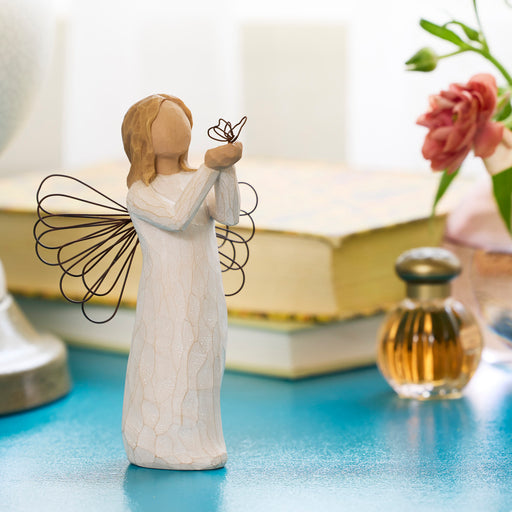 Angel figurine holding a butterfly on a blue surface with a book and flowers in the background