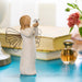 Angel figurine holding a butterfly on a blue surface with a book and flowers in the background