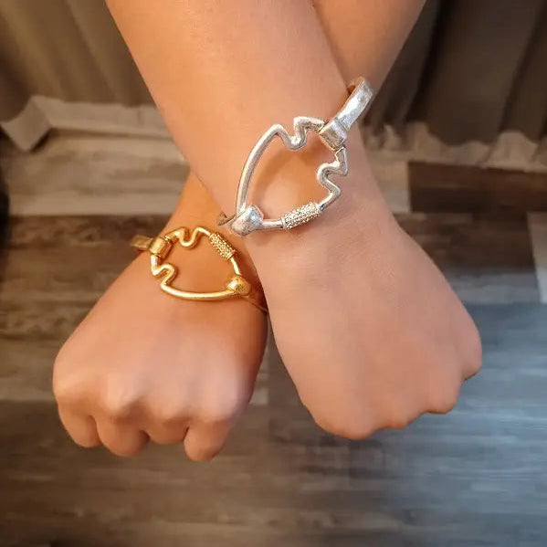 Two wrists wearing gold and silver heart-shaped bracelets against a blurred background.