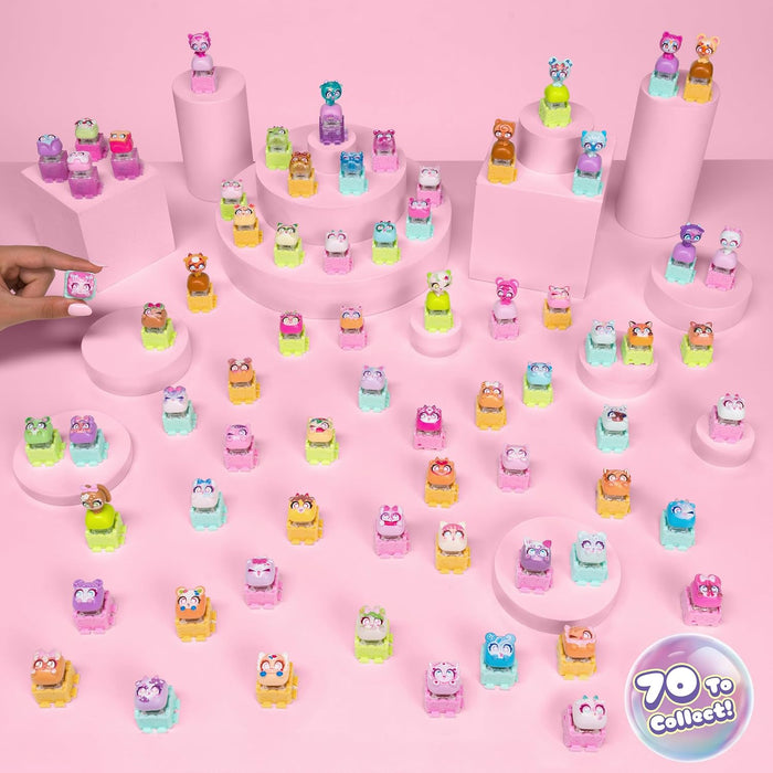 A collection of small colorful toy figurines displayed on pink pedestals and across a pink surface, with a hand placing one figurine on the left. A round badge in the bottom right reads '70 to collect!'.