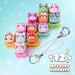 A set of 12 colorful 'Mystery Clickkeez' toy keychains arranged on a pastel blue background. The set includes various cute cat-themed clickers in pink, green, orange, and blue, along with two silver keychains with pink straps.
