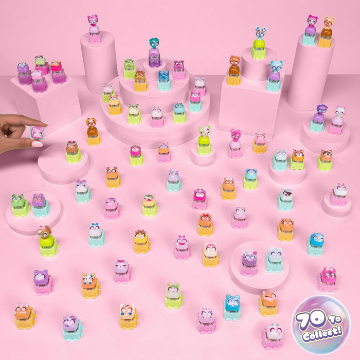 A collection of small colorful toy figurines displayed on pink pedestals and across a pink surface, with a hand placing one figurine on the left. A round badge in the bottom right reads '70 to collect!'.