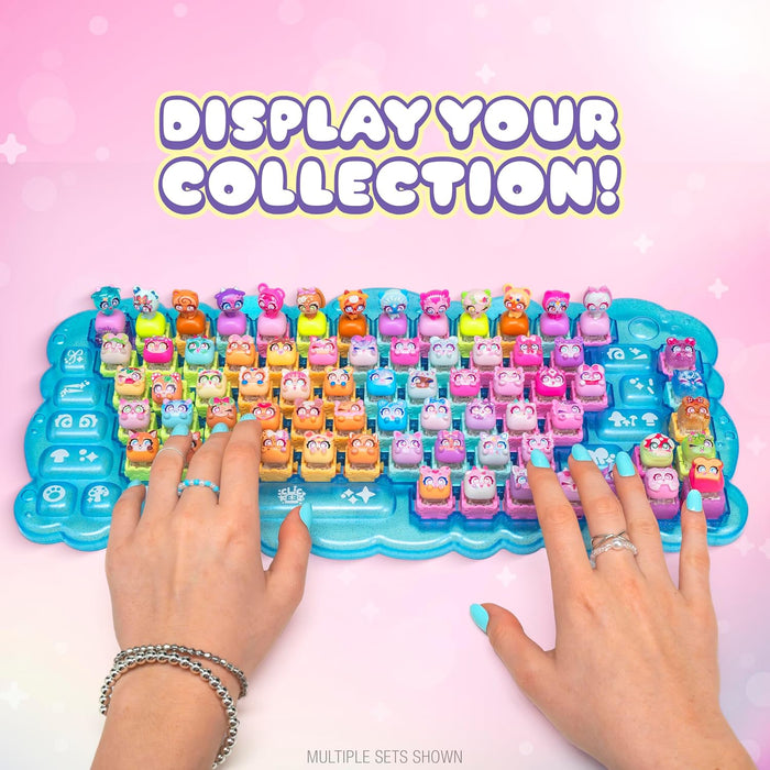 A hands-on promotional shot of a colorful toy keyboard with many small character-shaped keys. Two hands with turquoise nail polish are pressing the keys on a bright blue tray.