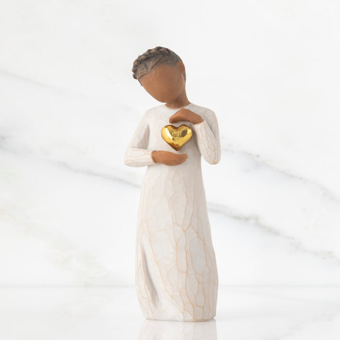 Figurine of a woman holding a gold heart against a white background