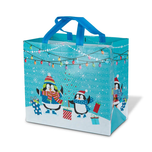A reusable holiday gift bag with blue handles, featuring a winter penguin design on a bright turquoise background with Christmas lights, snowflakes, and the words 'Happy Holidays' printed across the surface.
