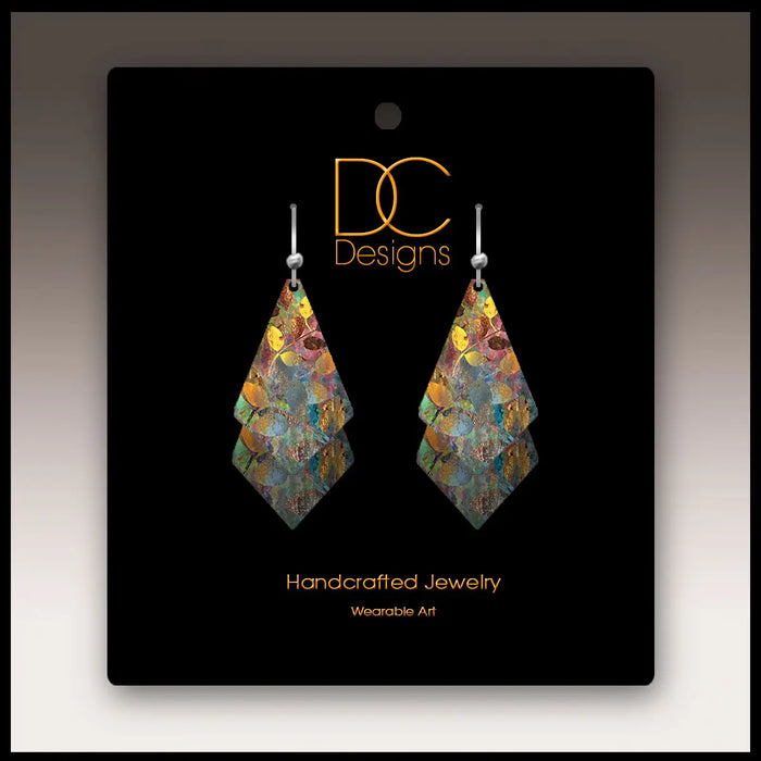 Colorful earrings on a black card with 'DC Designs' branding
