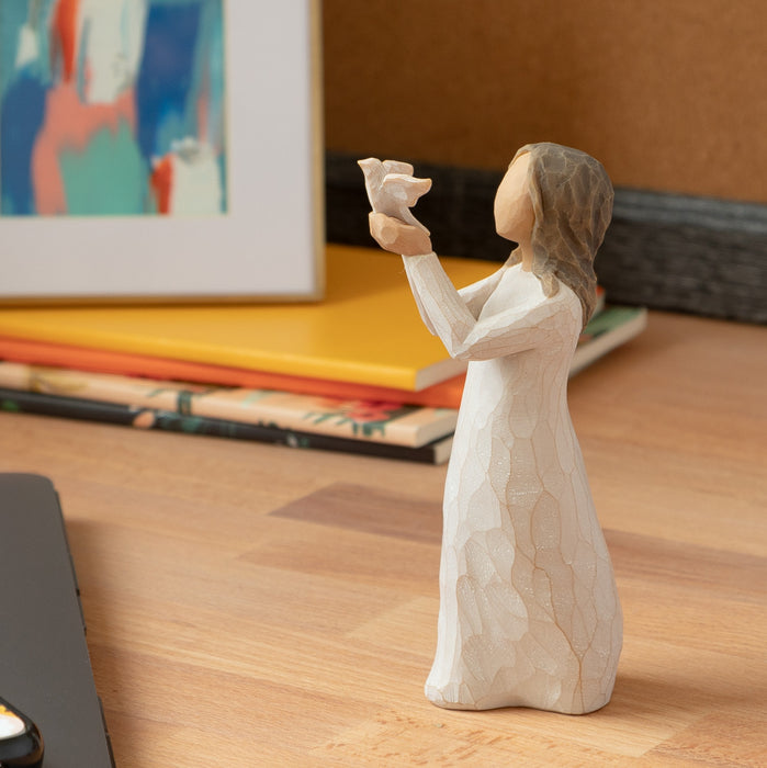Decorative figurine of a woman holding a teddy bear on a wooden surface with books and a painting in the background.