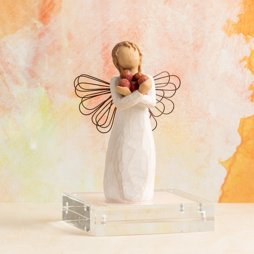 Angel figurine holding apples against a soft, multicolored background