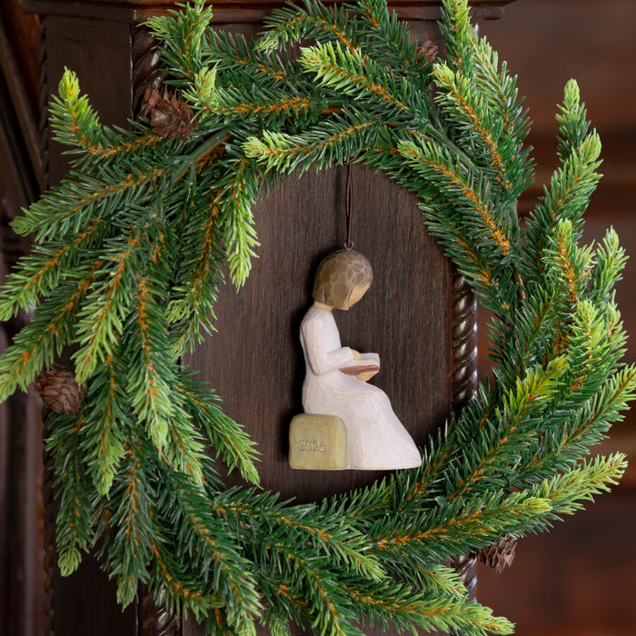 Decorative wreath with a figurine of a person sitting on a book inside, against a wooden background.