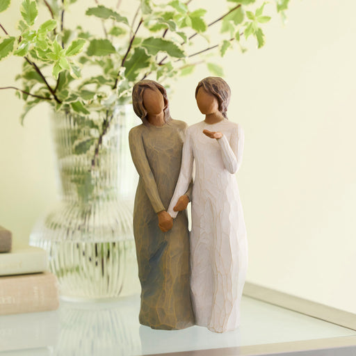 Two figurines woman holding hands with a vase of flowers in the background.