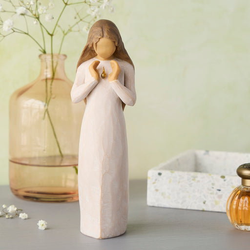 Decorative figurine of a woman holding a heart, with a vase and flowers in the background.