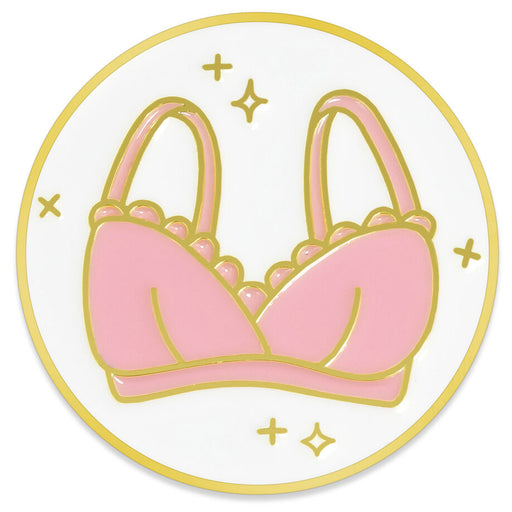 A circular enamel pin featuring a pink bra illustration with gold outlines on a white background.