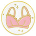 A circular enamel pin featuring a pink bra illustration with gold outlines on a white background.