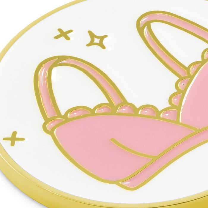 A close-up of a round white enamel pin or sticker featuring a pink bunny silhouette outlined in gold, with small gold stars and accents on a white background.