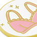 A close-up of a round white enamel pin or sticker featuring a pink bunny silhouette outlined in gold, with small gold stars and accents on a white background.