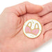 Pin with pink bra design held in a hand on a white background