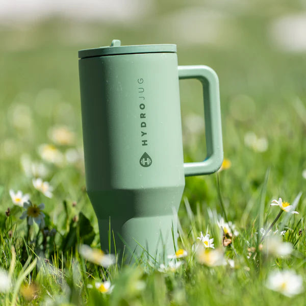 Green HydroJug tumbler in a grassy field with flowers