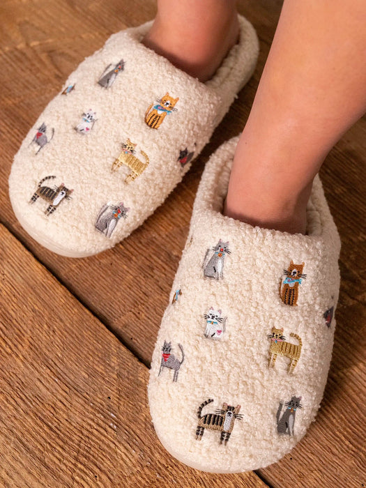 Beige slippers with embroidered cat designs on a wooden floor