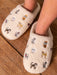 Beige slippers with embroidered cat designs on a wooden floor
