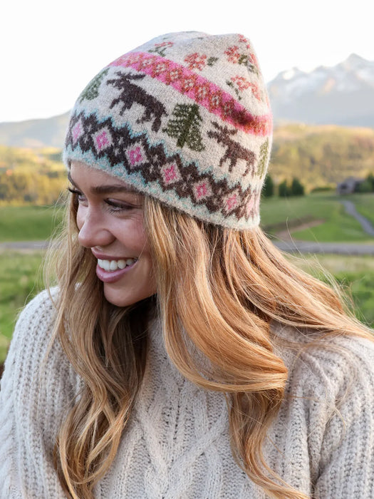 Woman wearing a knitted hat with moose and floral patterns in a natural setting.