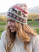 Woman wearing a knitted hat with moose and floral patterns in a natural setting.