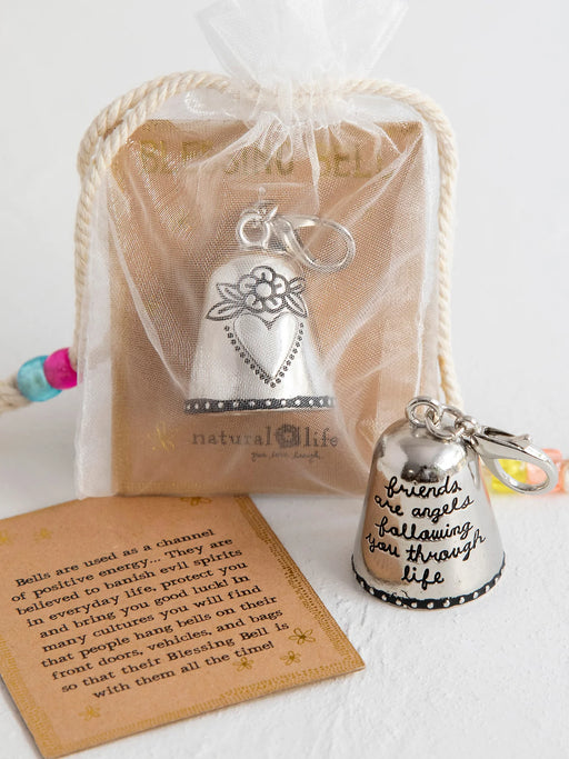 Silver bell keychain with engraved text, placed on a white surface with a sheer bag and card.