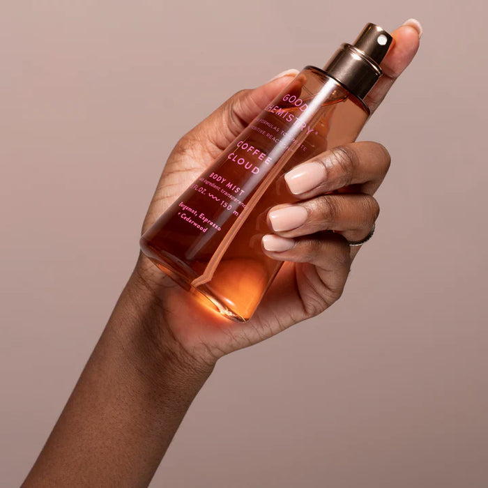 Hand holding a bottle of 'Good Marmite Coffee Cloud' body mist against a beige background