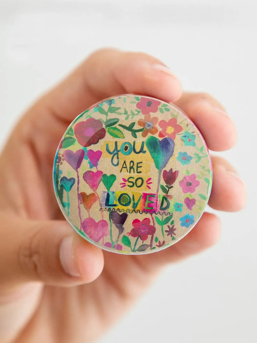 Hand holding a colorful round sticker with floral designs and text on a white background