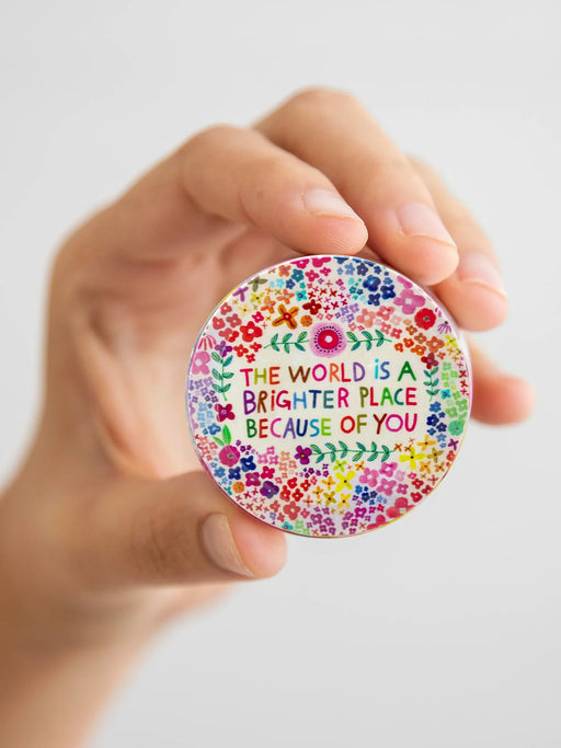 Hand holding a colorful circular sticker with text and floral design on a white background