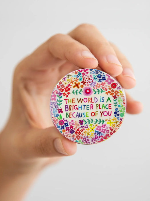 Hand holding a colorful circular sticker with text and floral design on a white background