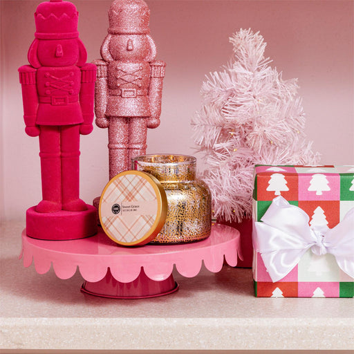 Decorative items including pink nutcrackers, candles, and a gift box on a pink stand with a pink background.