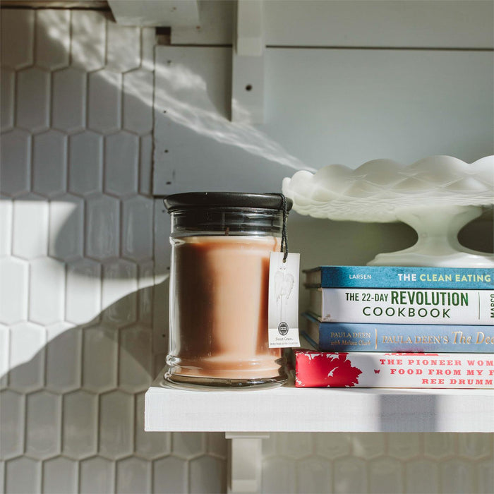 Candle in a glass jar with a tag on a shelf with books and a decorative shell.