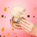 Hand holding a decorative item with a pink background and confetti