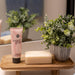 Bathroom setting with a pink tube of 'sweet grace' hand cream, a bar of soap, and a potted plant on a wooden tray.