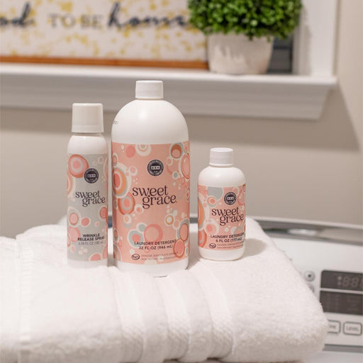 Bottles of 'sweet grace' products on a stack of white towels with a laundry room background.