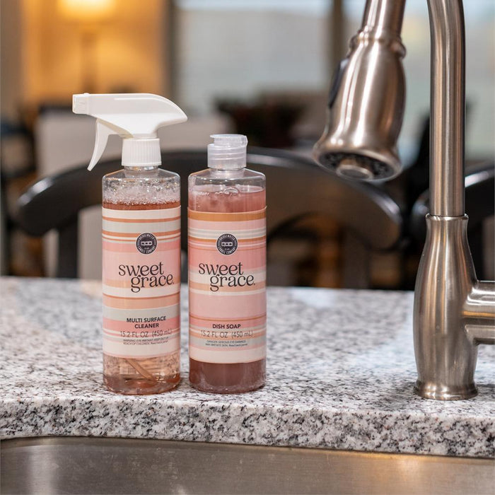 Two bottles of 'Sweet Grace' cleaning products on a kitchen counter with a faucet in the background.