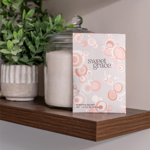 Sweet Grace scented sachet on a wooden shelf with plants and a jar.