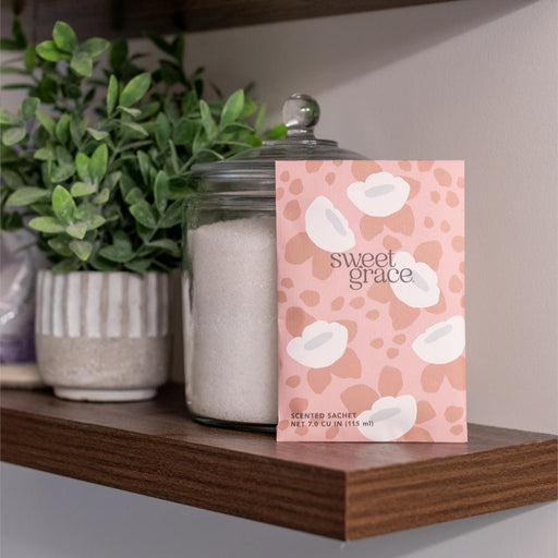 Shelf with a 'sweet grace' product packaging, plants, and a jar.