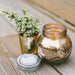 Decorative glass jar with candle, small potted plant, and lid on a wooden surface