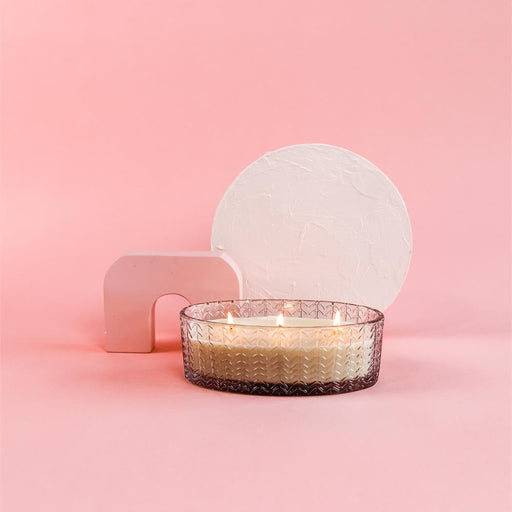 Candle in a glass holder with a white sphere on a pink background