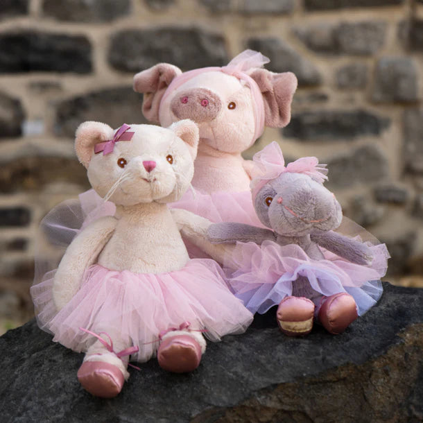 Three plush toys, including a bear, pig, and elephant, wearing tutus, sitting on a stone surface with a stone wall background.